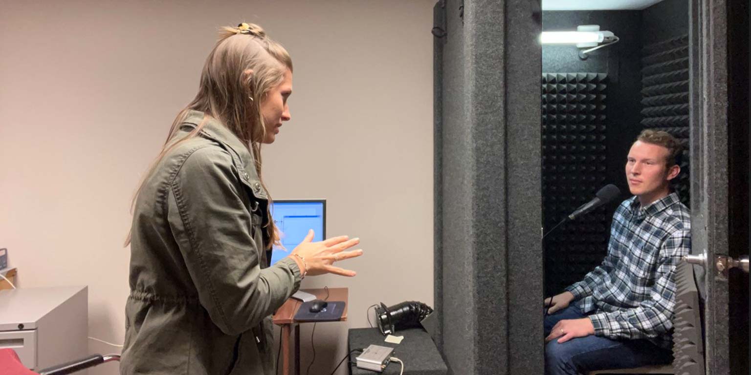 Student speaking with another student in a microphone booth